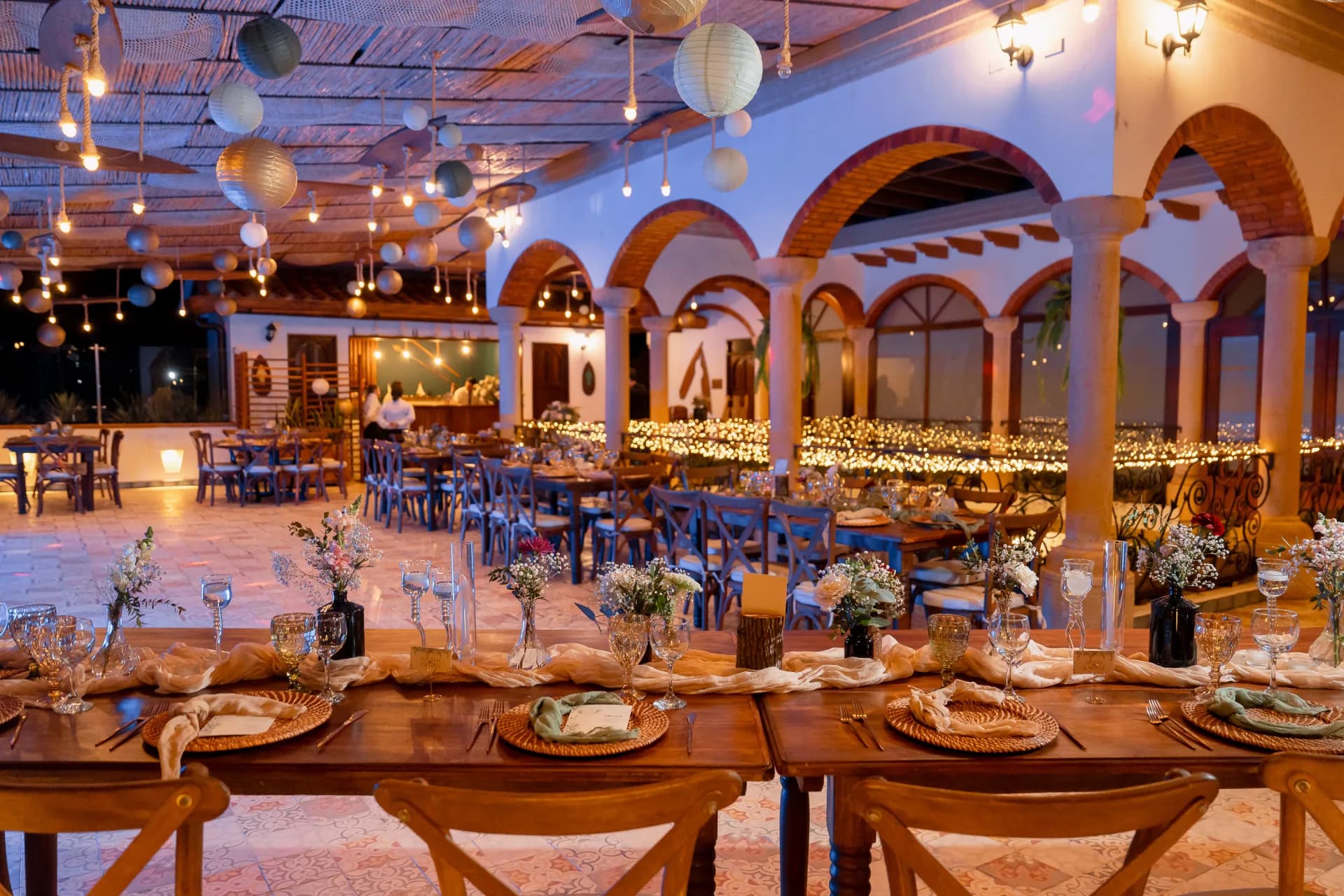 Long tables set under paper lanterns and string lights at dusk
