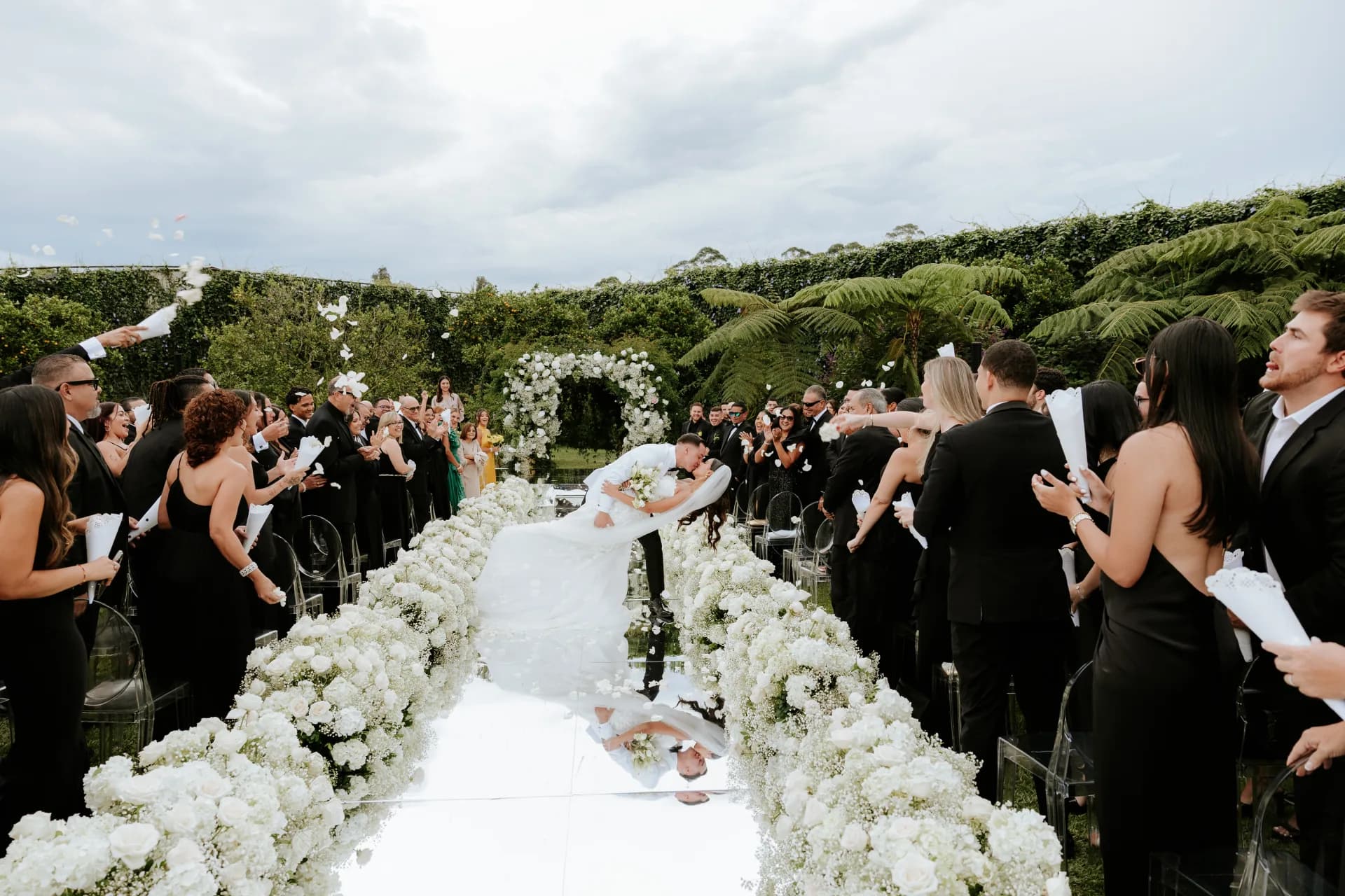 Bride and groom kissing at the end of the aisle while their guests throw petals